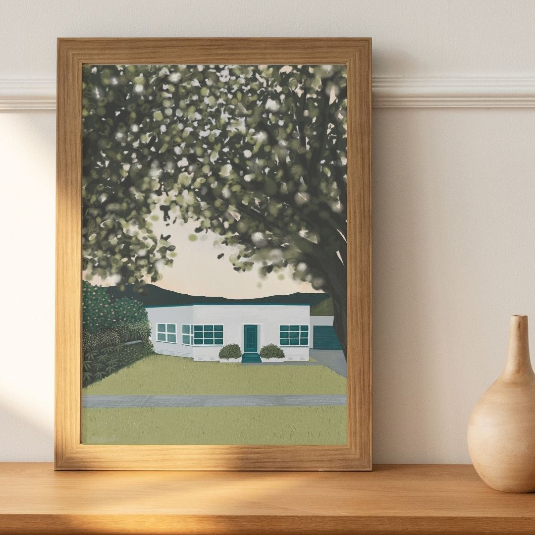 Framed artwork of a house under a tree on a wooden shelf.