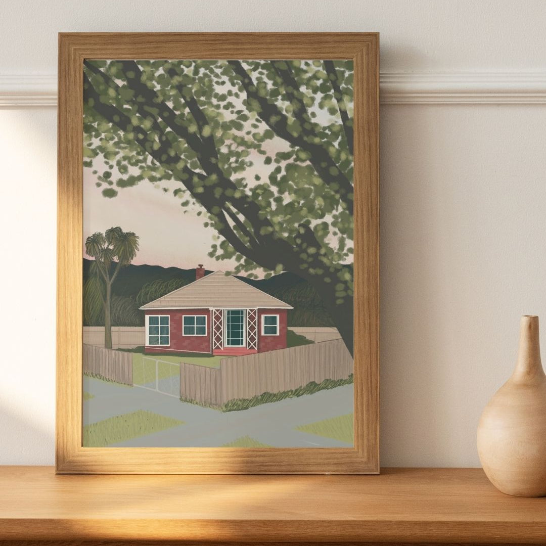Framed artwork of a house with trees on a wooden shelf.